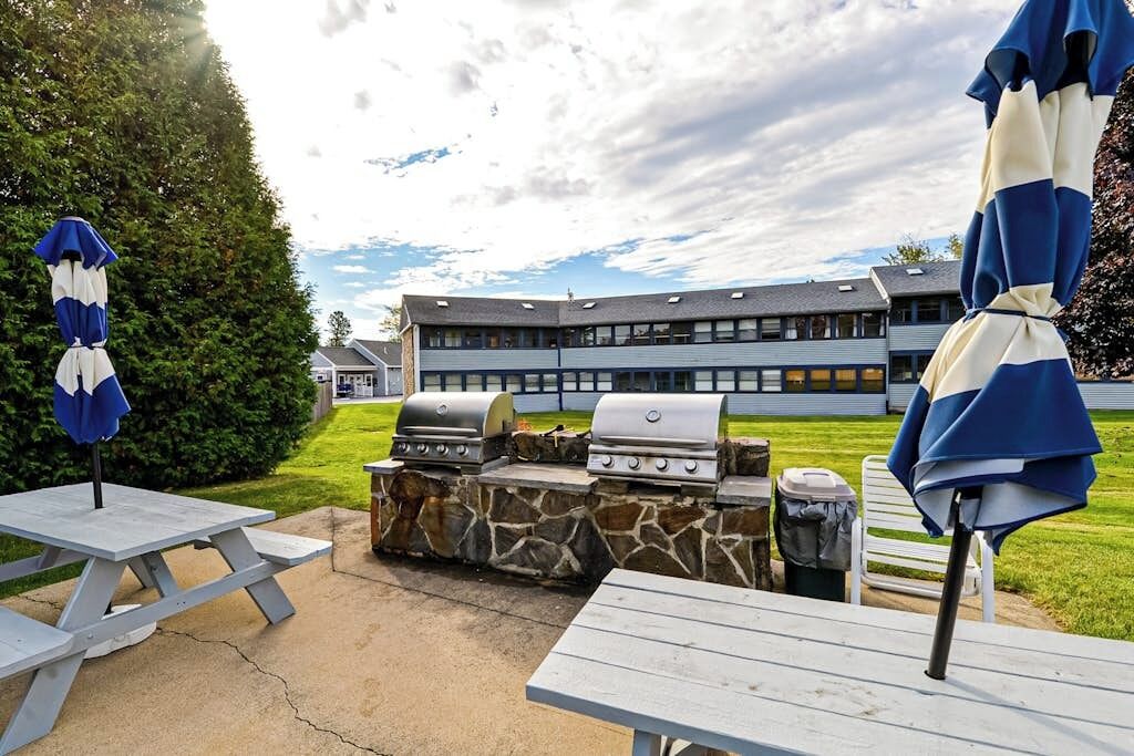 Une terrasse extérieure avec des tables de pique-nique, un barbecue et des parasols.