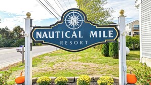 A sign for Nautical Mile Resort with a compass logo, surrounded by a landscaped area with plants and a mailbox. - Updated condo 1 mile to beach w/pool, hot tub, tennis & access to EV chargers! (Wells)