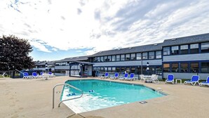 A swimming pool with lounge chairs, a covered seating area, and a building with large windows. - Updated condo 1 mile to beach w/pool, hot tub, tennis & access to EV chargers! (Wells)