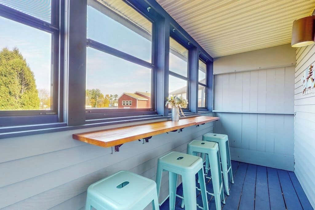A bar area with a wooden counter, light blue stools, and large windows.