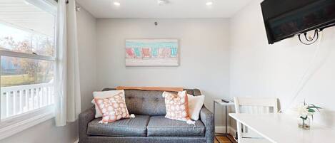 Una sala moderna con un sofá gris, una mesa de comedor blanca y un televisor de pantalla plana montado en la pared.