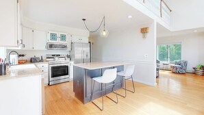 Una cucina moderna con isola centrale, elettrodomestici in acciaio inossidabile e zona pranzo con soffitto alto e scala.