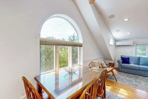 A modern interior with a dining table, chairs, a sofa, and large windows. - Inviting home with ocean view, firepit, deck, golf nearby, & W/D (York)