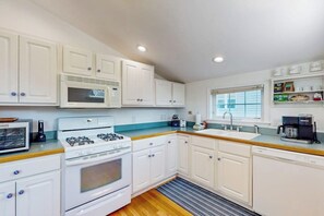 A kitchen with white cabinets, a stove, microwave, and a sink.