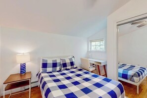 Ein Schlafzimmer mit karierter Bettdecke, einem Schreibtisch, einem Stuhl, einer Lampe und einem Fenster.