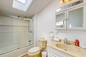 Ein Badezimmer mit Glasdusche, Toilette, Waschbecken und einem Spiegel darüber sowie einem Oberlicht.