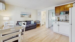 Un espace de vie compact comprenant un coin repas, un canapé, une cuisine avec des meubles blancs et un tableau accroché au mur.