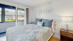Une chambre à coucher avec un lit, une table de chevet, une lampe et une fenêtre donnant sur l’extérieur.