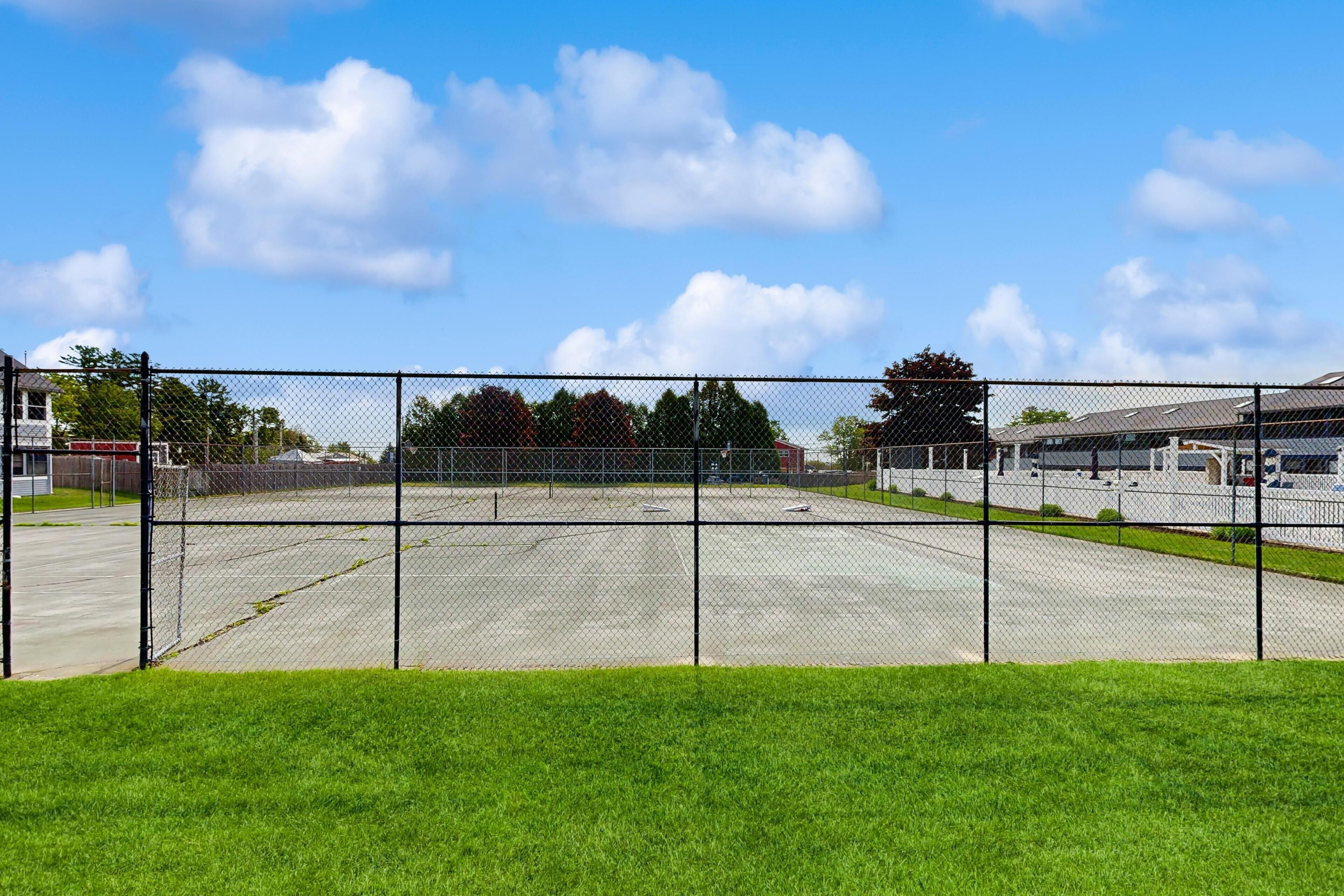 En indhegnet tennisbane med klar himmel og bygninger i baggrunden.