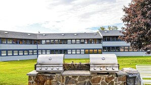 Un barbecue en pierre doté de deux brûleurs, installé devant un bâtiment à toit plat et aux grandes fenêtres.