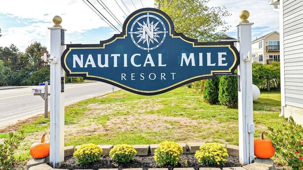 Une enseigne pour le Nautical Mile Resort, avec un symbole de boussole, entourée d’un espace paysager agrémenté de plantes et d’une boîte aux lettres.
