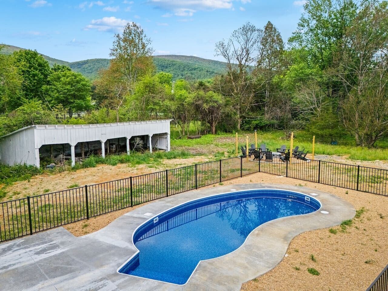 A swimming pool with a curved edge, surrounded by a black metal fence, and a white building in the background.