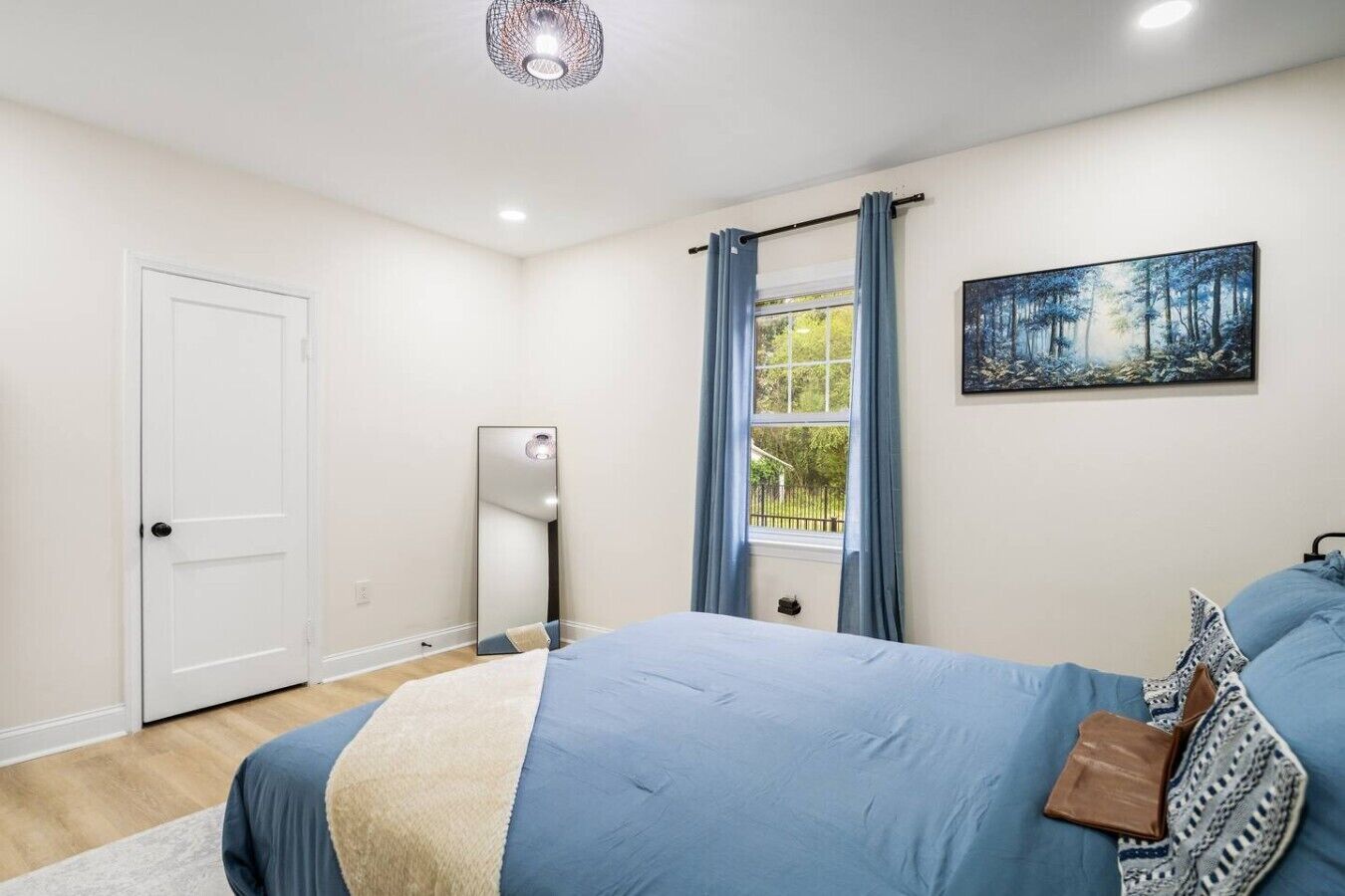 Een slaapkamer met een bed, een raam met gordijnen, een spiegel en een schilderij aan de muur.