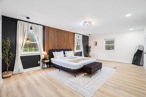 A modern bedroom with a large bed, a bedside table, a nightstand, a mirror, and a window with curtains.