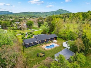 A large house with a swimming pool, surrounded by lush greenery and hills in the background.