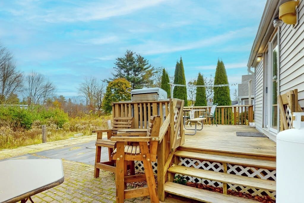 A wooden deck with outdoor furniture, a covered seating area, and a view of trees and a building in the background.