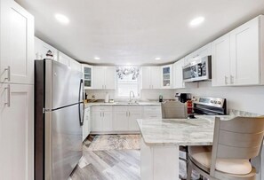 A modern kitchen with white cabinetry, a stainless steel refrigerator, a microwave, and a dining area with a marble countertop and chairs. - Adorable nautical home close to town, W/D, & streaming, dog friendly (Wells)