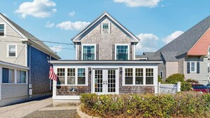 Ein zweistöckiges Haus mit Giebeldach, einer Veranda und einer kleinen amerikanischen Flagge.