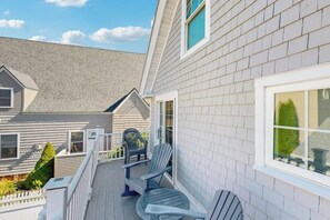 Ein Wohngebäude mit Balkon, zwei Adirondack-Stühlen und einem Fenster mit Aussicht.