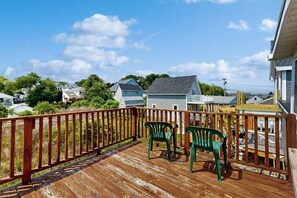 Une terrasse en bois avec deux chaises vertes, une rambarde et des maisons en arrière-plan.