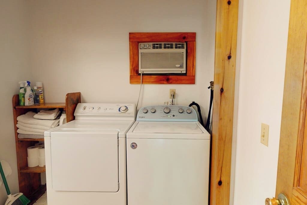 A laundry area with two stacked washers and dryers, a wooden shelf with folded towels, and a wall-mounted heater.