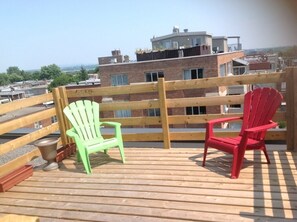 Eine Holzterrasse mit zwei Adirondack-Stühlen, einer Geländer und Blick auf Gebäude im Hintergrund.