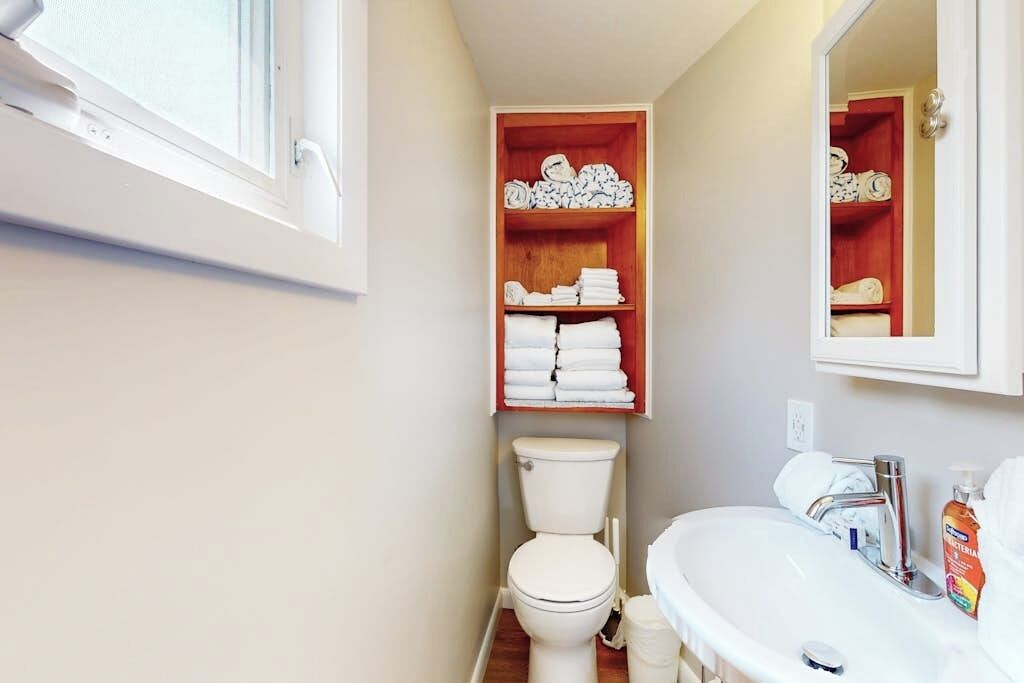 A bathroom with a toilet, a sink, and a shelf with folded towels.