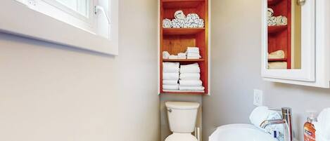 A bathroom with a toilet, a sink, and a shelf with folded towels.