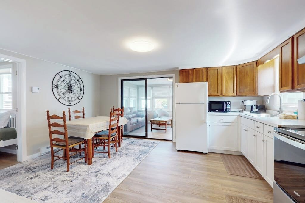 A modern kitchen with white cabinets, a refrigerator, microwave, and a dining area with a table and chairs.