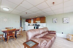 Un salon avec un canapé en cuir marron, une table à manger en bois avec des chaises, et une cuisine en arrière-plan.