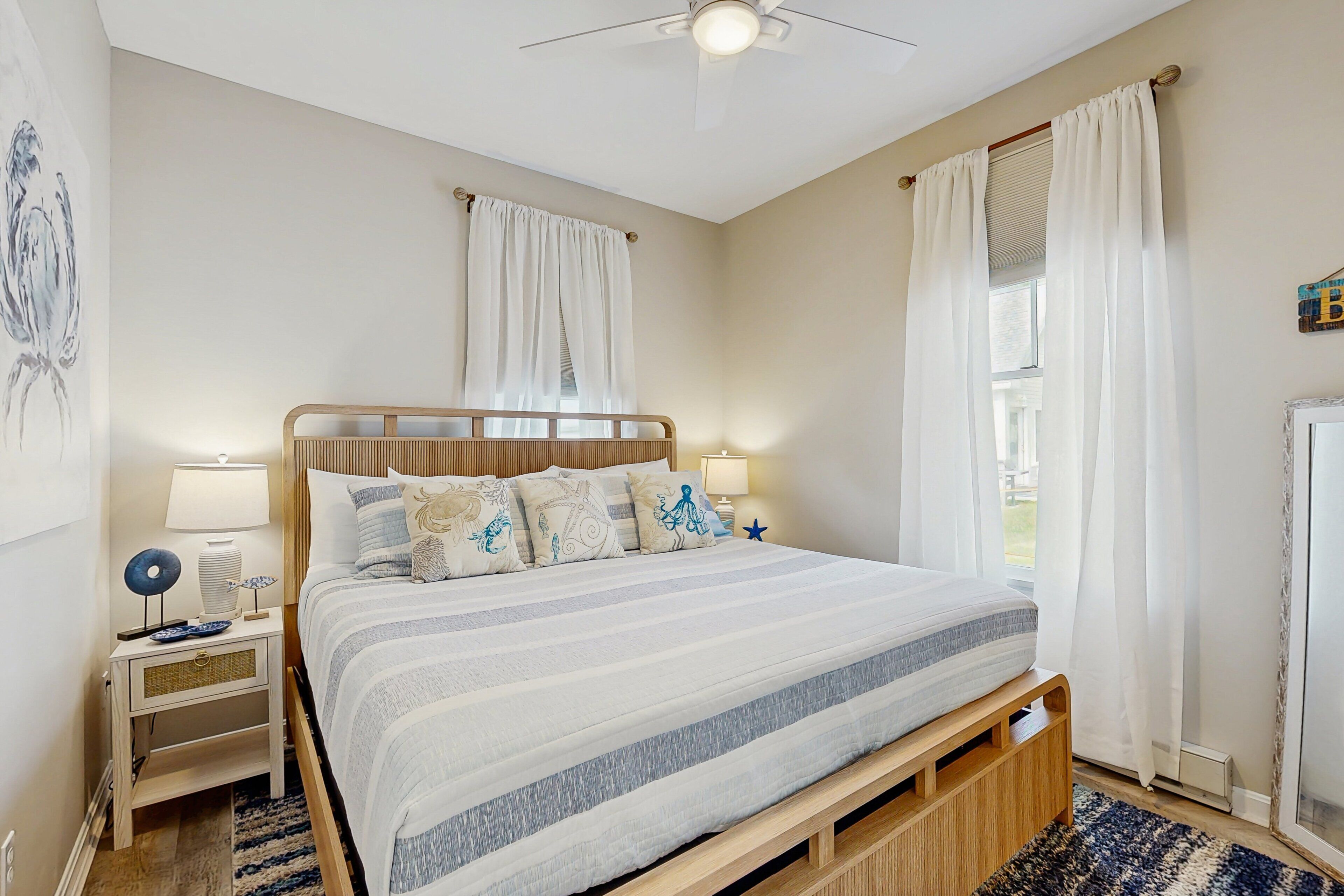 Un dormitorio con cama, mesitas de noche, ventilador de techo y ventana con cortinas.