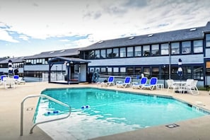 Ein Pool mit Liegestühlen und einem überdachten Bereich, neben einem Gebäude mit großen Fenstern.