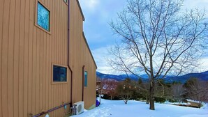 A wooden building with large windows, a snow-covered ground, and a tree in the foreground. - Beautiful townhome w/ mountain views from the deck, near skiing (Bartlett)