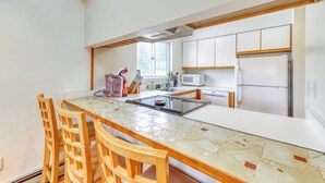 A kitchen with a central island, wooden chairs, a microwave, and a refrigerator. - Beautiful townhome w/ mountain views from the deck, near skiing (Bartlett)