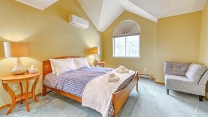 A bedroom with a bed, two bedside tables, a chair, a window, and an air conditioning unit. - Beautiful townhome w/ mountain views from the deck, near skiing (Bartlett)