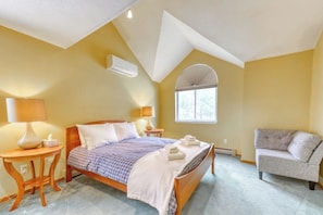 Ein Schlafzimmer mit einem Bett, zwei Nachttischen, einem Sessel, einem Fenster und einer Klimaanlage.