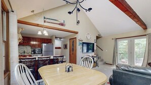 Een eethoek met een tafel en stoelen, een keuken op de achtergrond en een zithoek met een bank en televisie.