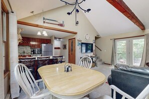 A dining area with a table and chairs, a kitchen in the background, and a living area with a couch and a TV. - Cozy townhome with gas grill, jetted tub & gas fireplace - 1 mile to Story Land (Bartlett)