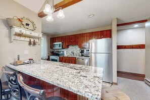 A kitchen with a granite countertop, wooden cabinets, a refrigerator, and a microwave. - Cozy townhome with gas grill, jetted tub & gas fireplace - 1 mile to Story Land (Bartlett)