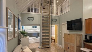 Un espace de vie de style loft comprenant un lit superposé, un téléviseur, une armoire en bois et un escalier.