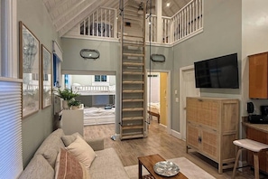 A loft-style living area with a bunk bed, a TV, a wooden cabinet, and a staircase. - Cozy cottage with steps-to-the-pool access, fully equipped kitchen & beach gear (Wells)