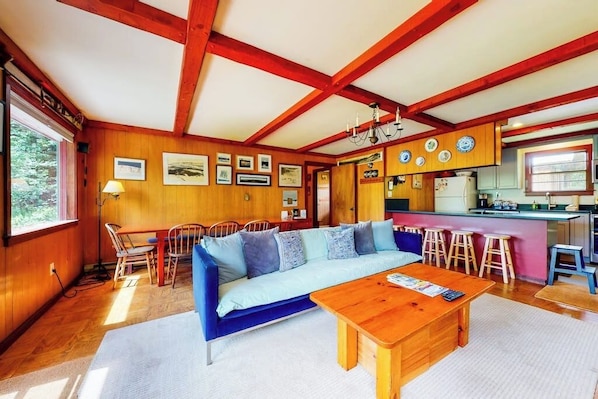 A cozy living room with a sofa, wooden coffee table, and a dining area with chairs and stools.