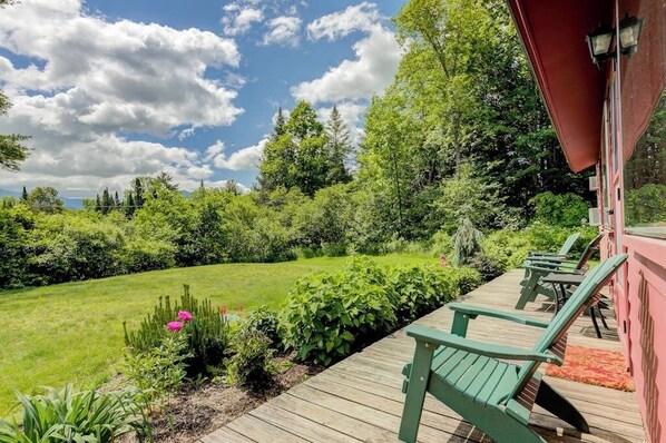 Une terrasse en bois avec des chaises vertes, une pelouse et un bâtiment rouge.
