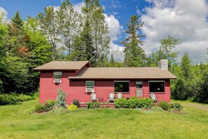 Une maison rouge avec un toit marron, entourée de verdure et d’arbres.