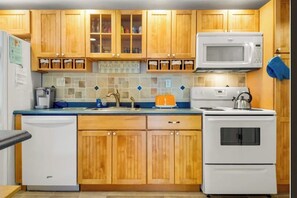 A kitchen with wooden cabinets, a microwave, an oven, a dishwasher, and a tiled backsplash. - Coastal Wells Beach Condo | Walk to the Ocean | Family-Friendly (Wells)