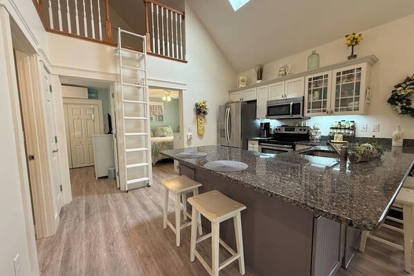 A kitchen with a granite countertop, white cabinets, a stainless steel refrigerator, and a microwave.