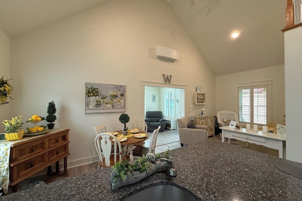 A kitchen with granite countertops, a dining area with a table and chairs, a living room with a sofa and chairs, and a hallway leading to a door.