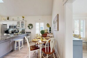 A kitchen with white cabinets, a dining table with chairs, a microwave, and a refrigerator.