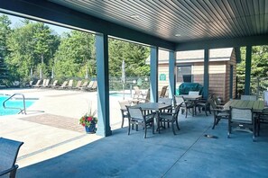 A covered outdoor area with a pool, lounge chairs, and tables.