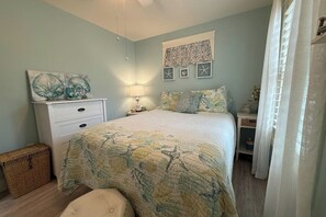 A bedroom with a bed, a dresser, a nightstand, a lamp, and wall art.